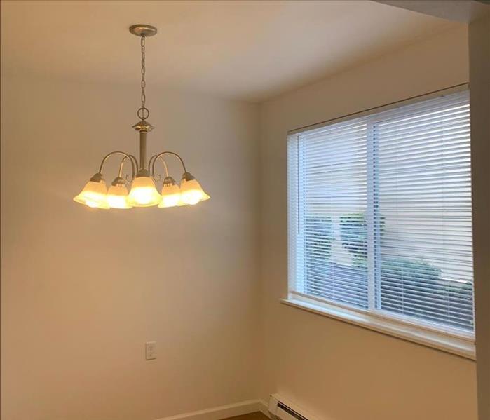A repainted dining room without contents. It is decorated with a chandelier, new window blinds, clean wood flooring, baseboar